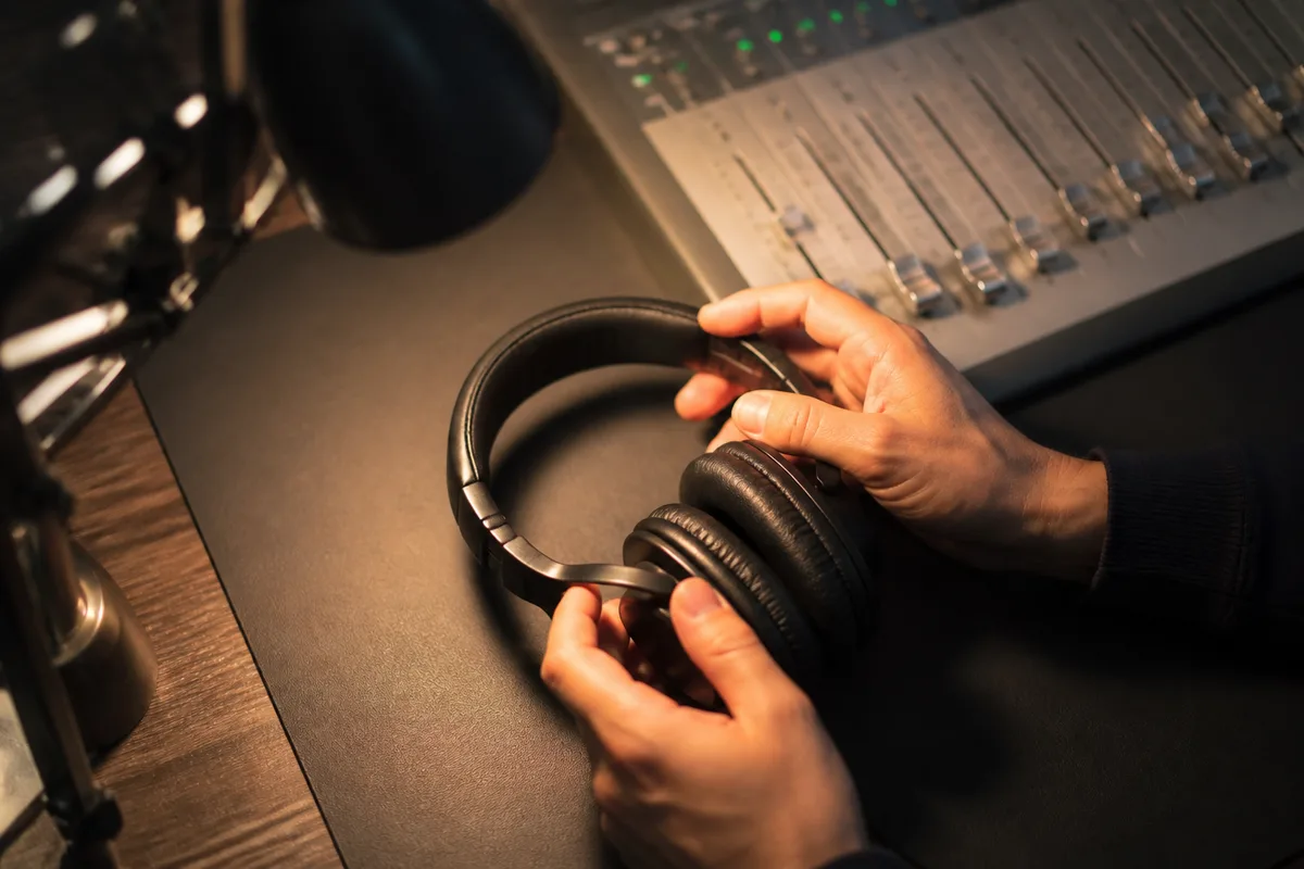 Mains ajustant un casque audio de studio posé près d’un clavier, lumière chaude